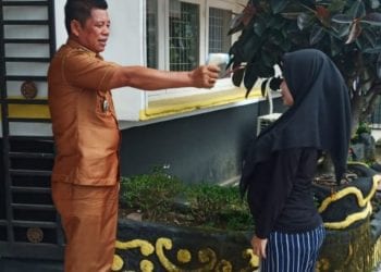 Camat Rantau Utara Turing Ritonga saat melakukan pengecekan suhu badan warga yang datang.