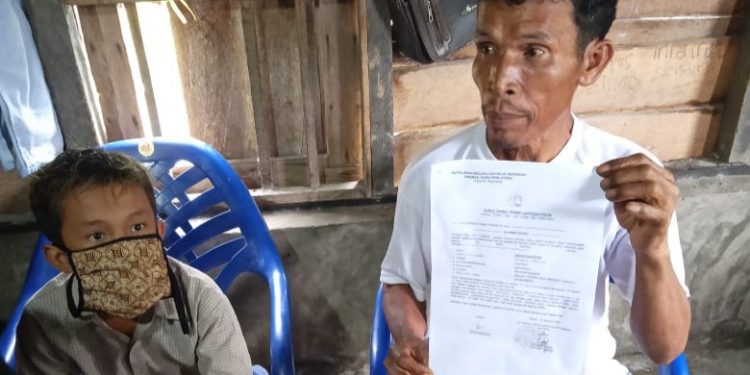 Aron Panjaitan menunjukkan surat laporan kasus penganiayaan terhadap anaknya yang dilakukan 5 pria warga desa yang sama.