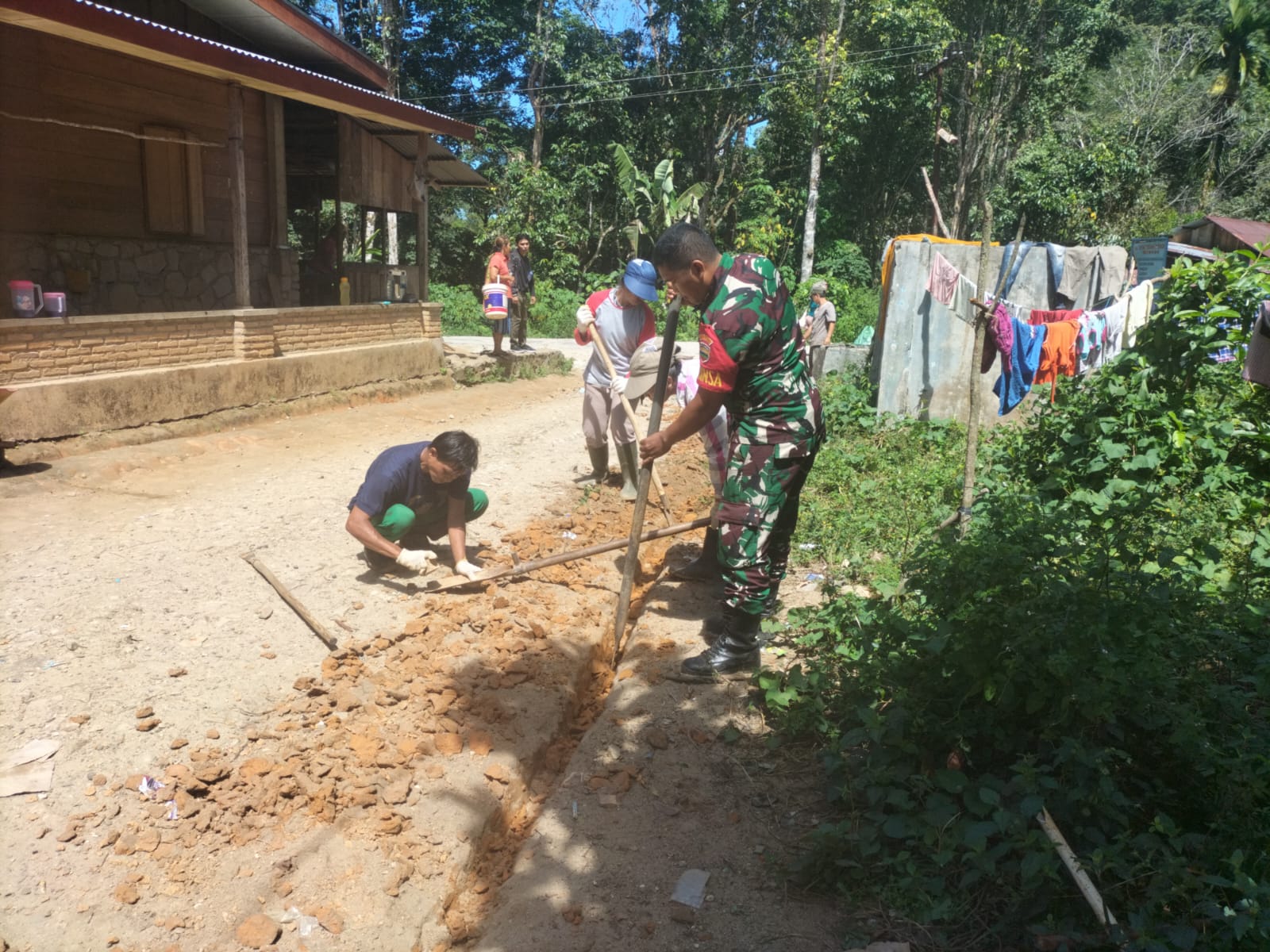 Babinsa Koramil 05/Kolang, Serda Rondang Martua Manullang membantu warga menggali saluran pipa air bersih, di Desa Naga Timbul, Kabupaten Tapteng. 